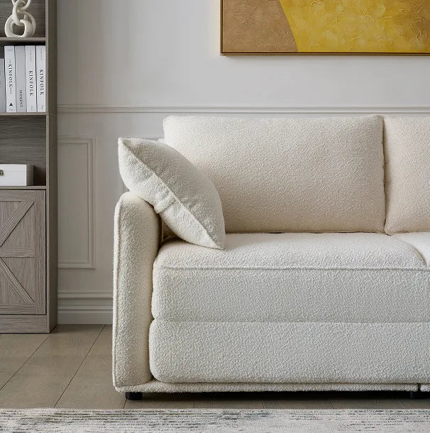 Cream boucle Sunset Sofa Bed with plush armrest cushion beside a styled bookshelf.