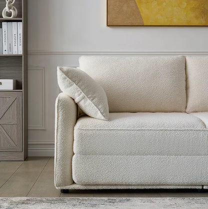Cream boucle Sunset Sofa Bed with plush armrest cushion beside a styled bookshelf.