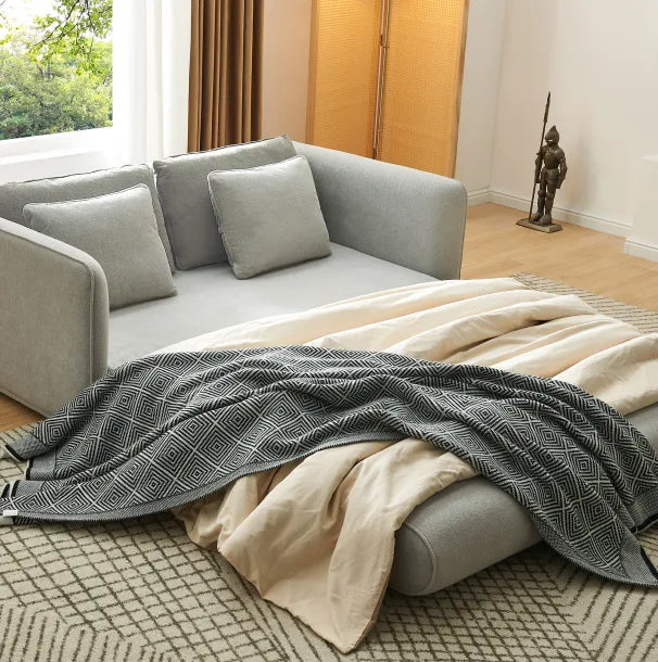 Grey Sunset Sofa Bed extended into a sleeper with woven throw and cushions in a sunlit room.