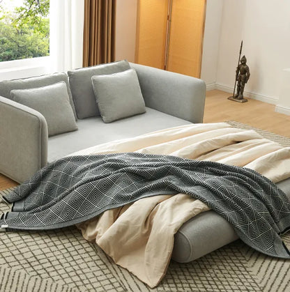 Grey Sunset Sofa Bed extended into a sleeper with woven throw and cushions in a sunlit room.